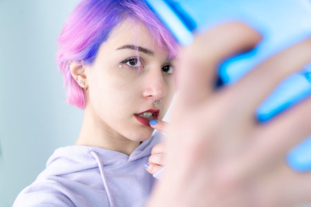 A young woman with blue and pink hair is taking a selfie with her cell phone. Generation z woman...