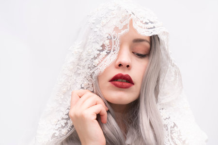 A woman with long gray hair and red lipstick is wearing a white veil