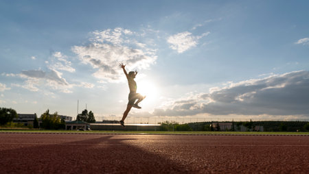 Silhouette of a young woman jumping on a track at sunsetの写真素材