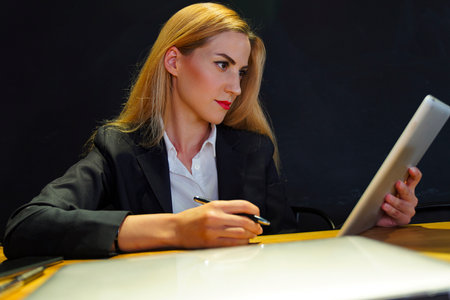 A woman in a business suit sits at a desk with a laptop. modern businesswoman working with laptop in officeの写真素材
