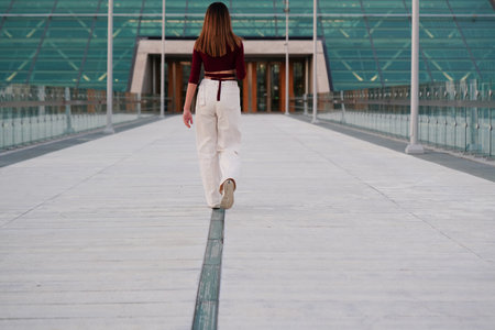 young woman walks past a glass building,
