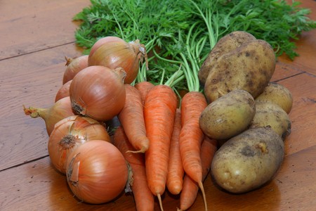 A selection of root vegetables onions, carrots and potatoes on a wooden kitchen tableの写真素材