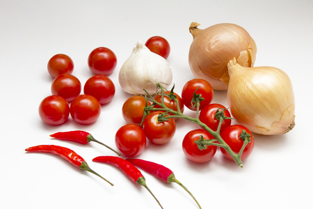 An arrangement of onons, tomatoes, chillies and garlic on a white backgroundの写真素材