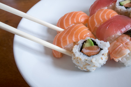 Fresh salmon nigiri sushi between chopsticks along with uramaki, prawn nigiri and tuna nigiriの写真素材