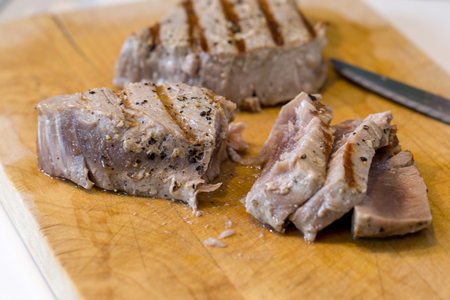 Chargrilled, seasoned tuna steaks cooked and sliced on a wooden chopping boardの写真素材