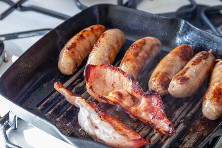 Cumberland sausages and back bacon cooking in a griddle panの写真素材
