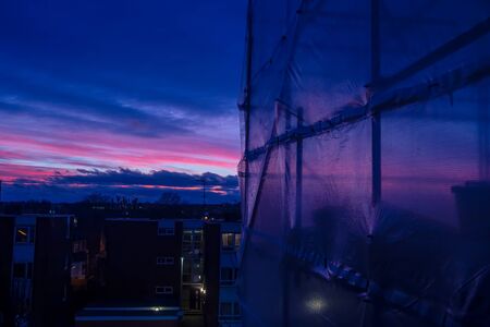 Scaffolding and protective cover sheets on a residential building at sunsetの写真素材