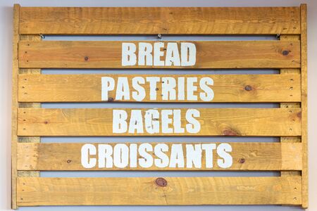 Bread, pastries, bagels and croissants. Baked breakfast goods advertised on a wooden sign board