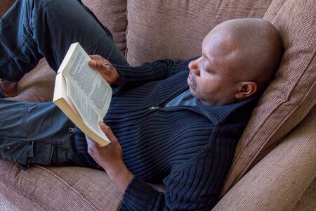 Black man, of African ethnicity, reading on the sofaの写真素材