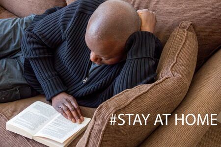Black man, of African ethnicity, reading on the sofa