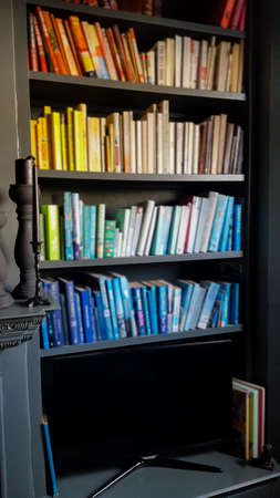 Dark bookcase, filled with blurred books organised by colour, in a home environmentの写真素材