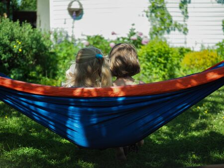 two little girls sitting in hammock in summer in garden rear viewの写真素材
