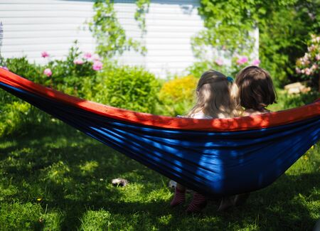 two little girls sitting in hammock in summer in garden rear viewの写真素材