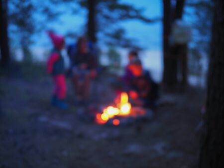 people and children sit around the campfire at night blurred viewの写真素材