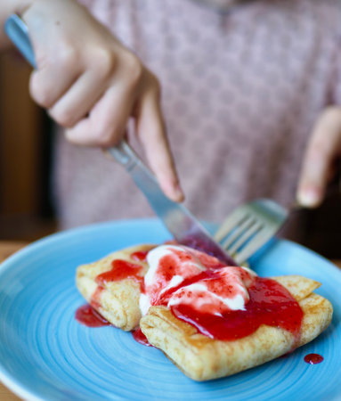 pancakes with jam and sour cream on a blue plate are eaten by a person.close-up.の写真素材