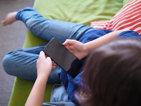 little Girl using touchscreen of a Smartphone. the child is sitting on the sofa using phoneの写真素材