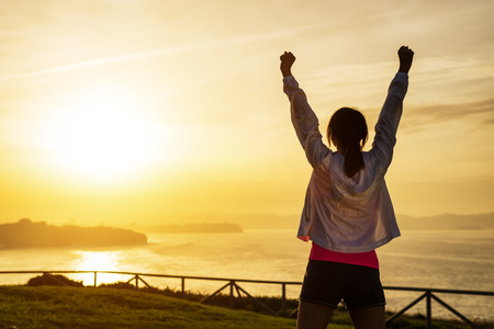 Successful sporty woman raising arms towards golden beautiful sunset and sea. Female athlete celebrating sport success and goals. Healthy lifestyle and freedom concept. Successful sporty woman raising arms towards golden beautiful sunset and sea. Female athlete celebrating sport success and goals. Healthy lifestyle and freedom concept.