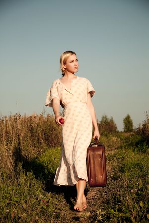 Young woman walking with suitcase in the field.の写真素材