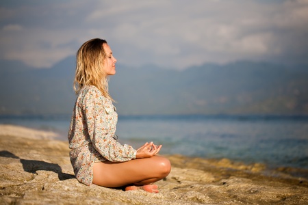 Woman sitting in lotus position on rock by the seaの写真素材
