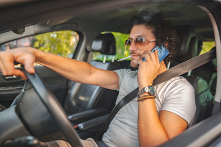 Man with curly hair driving a car, smoking a cigarette and using phone