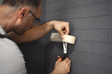 Man sticks protective tape on the wall before paintingの写真素材