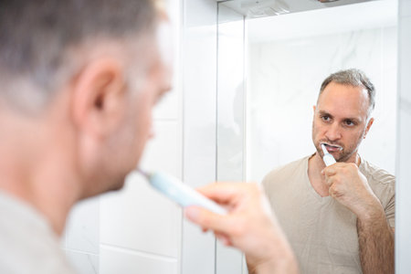 Man brushing his teeth with electric toothbrush in bathroomの写真素材