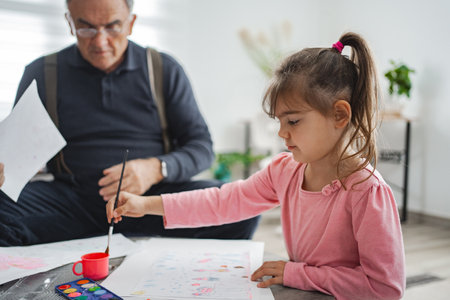 Grandpa and granddaughter painting at homeの写真素材