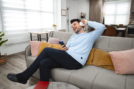 Man with wireless headphones listening to music in the living roomの写真素材