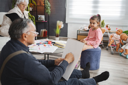 Grandfather draws a girl in a cozy living roomの写真素材