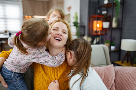 Three cute little girls hug, kiss and play with their momの写真素材