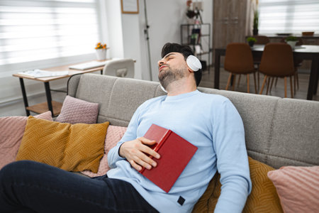 Man with wireless headphones fell asleep while reading a book at home