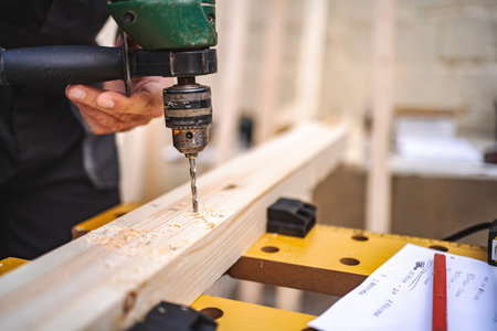 Unrecognizable male carpenter using electric drill on a wooden plank outdoorsの写真素材