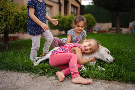 Children happily playing with a dog in a sunny gardenの写真素材