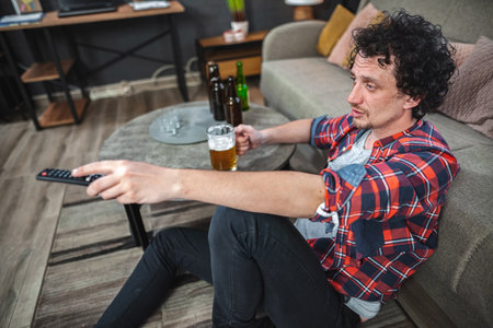 Young man drinking beer and watching tv at homeの写真素材