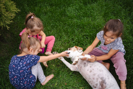 Children playing joyfully with a dog in a lush green gardenの写真素材