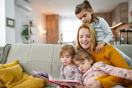 Mother looks at a book and reads a story to her daughtersの写真素材
