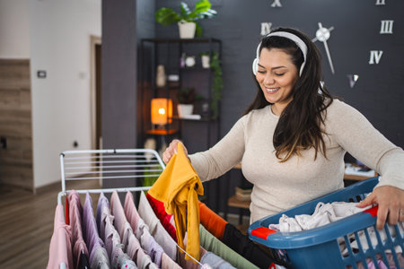 Woman listening to music while hanging the laundry on drying rack at homeの写真素材