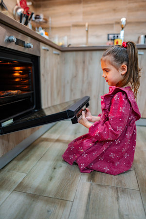 Little chef joyfully awaits baking treats in a cozy kitchen during a sunny afternoonの写真素材