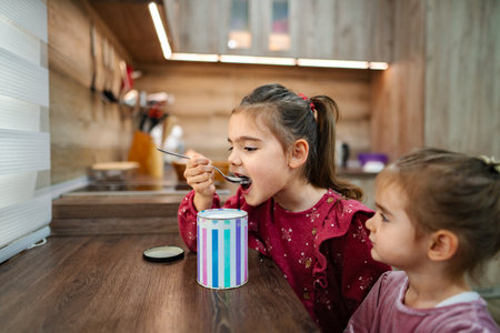 Two young sisters enjoy a sweet treat together at home in a cozy kitchen during the afternoonの写真素材