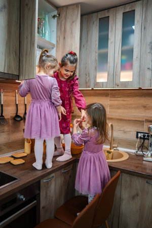 Lively moments of three girls joyfully playing in a cozy kitchen while preparing a fun snack together on a bright afternoonの写真素材