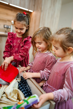 Three cheerful girls sharing a moment while exploring kitchen drawers filled with colorful items in a cozy home settingの写真素材