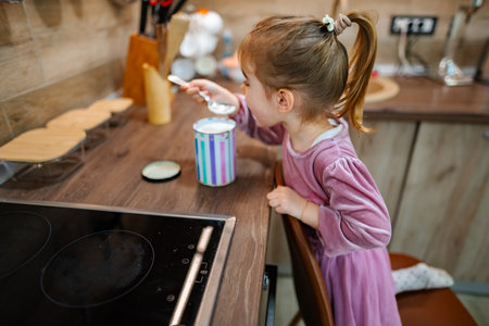 Young girl enjoying a sweet treat in a cozy kitchen during a sunny afternoonの写真素材