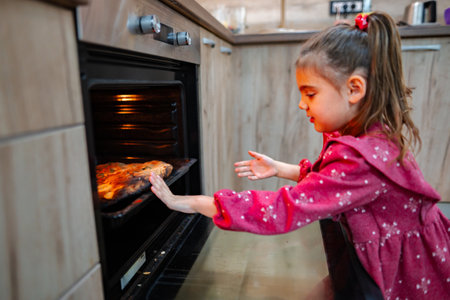 Excitement fills the kitchen as a young girl carefully removes a delicious homemade pizza from the oven in the heart of her cozy homeの写真素材