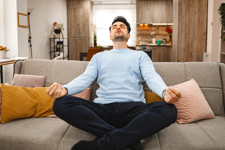 Brown-haired man sits on a couch and meditatesの写真素材