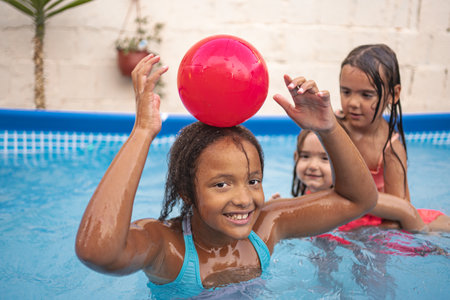 Children enjoying a sunny day playing with a red ball in a pool