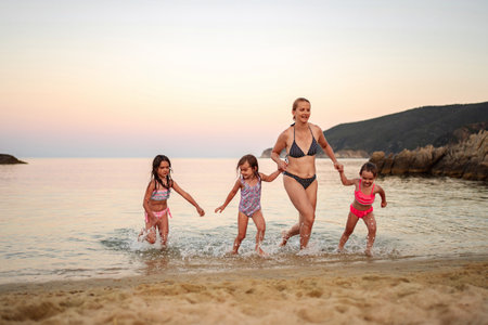 Joyful family splashes in the gentle waves at sunset on the beachの写真素材