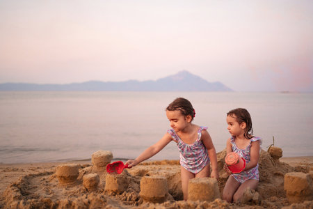 Sisters building sandcastles at sunset on a tranquil beachの写真素材