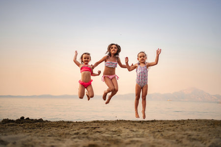 Joyful children jumping at sunset on a sandy beachの写真素材