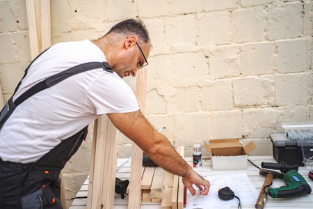 Mature male carpenter using electric screwdriver on a wooden plank outdoorsの写真素材
