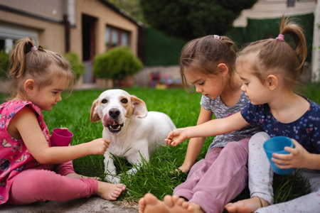 Joyful moments with a playful dog and children in a sunny gardenの写真素材